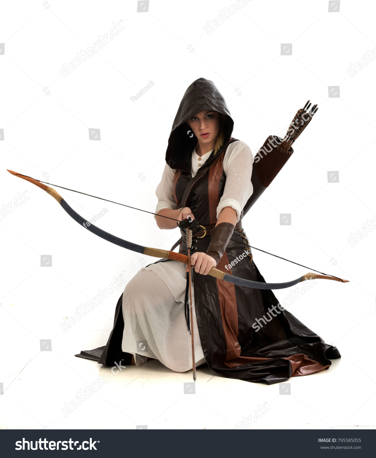 茶色のファンタジー衣装を着て 弓と矢を持つ女の子の全長のポートレート 白いスタジオ背景にひざまずくポーズ の写真素材 今すぐ編集