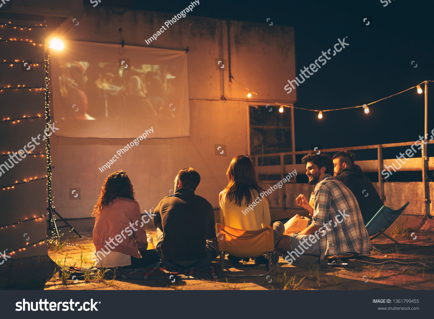 ビルの屋上のテラスで映画を見たり ポップコーンを食べたり ビールを飲んだり 楽しんだりする若い友人のグループ の写真素材 今すぐ編集