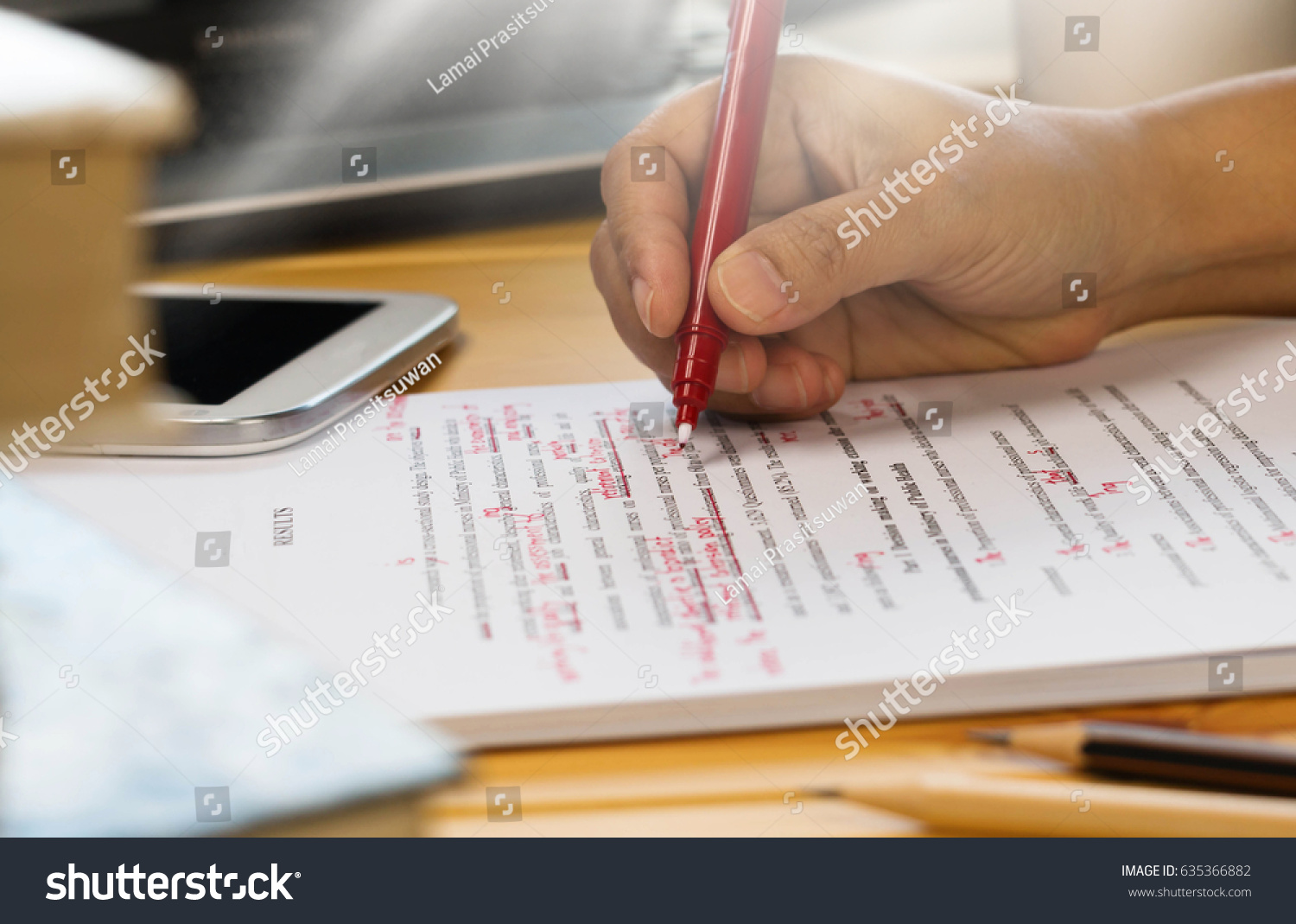 hand holding red pen over proofreading text in office