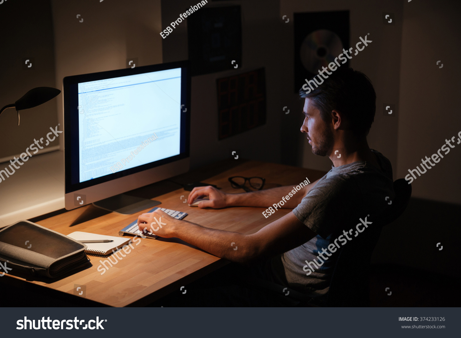 暗い部屋に座ってパソコンを使うハンサムな若者 の写真素材 今すぐ編集