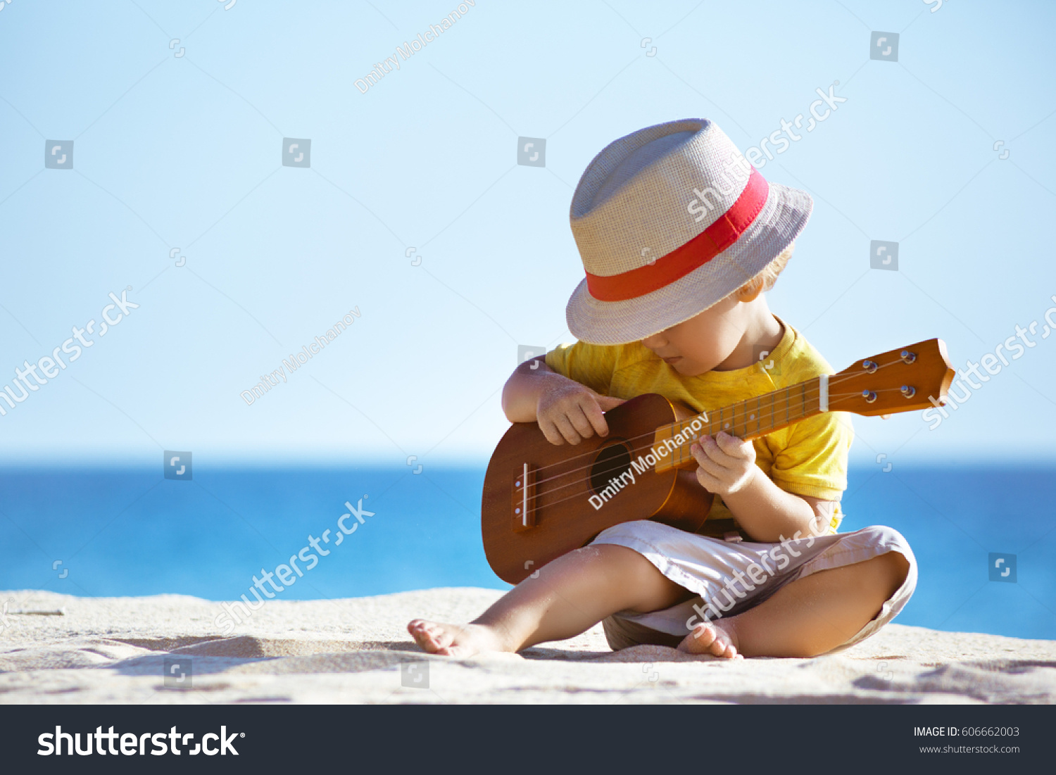 小さな男の子は 海岸の背景にハワイのギターやウクレレを弾きます テキストのスペース の写真素材 今すぐ編集