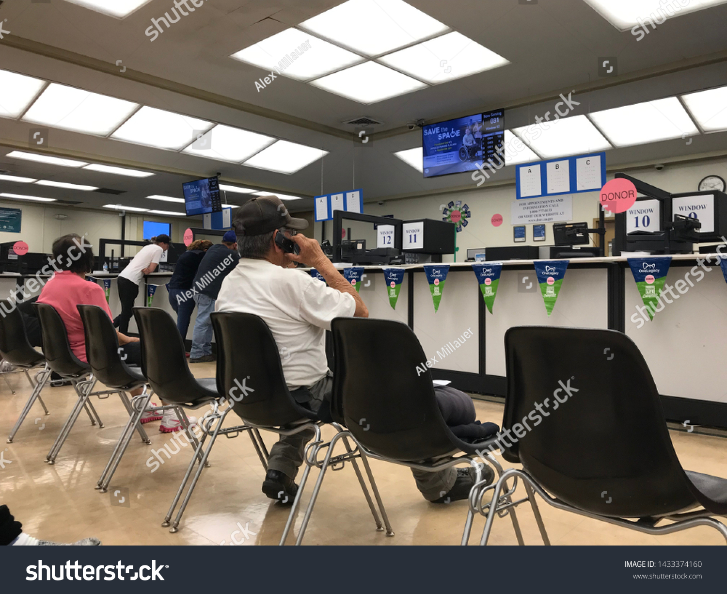 LOS ANGELES, April 25, 2019: DMV Department of Motor Vehicles Culver City interior. Latino man talking on his cell phone while sitting on a chair, waiting his turn, near the counter inside the DMV