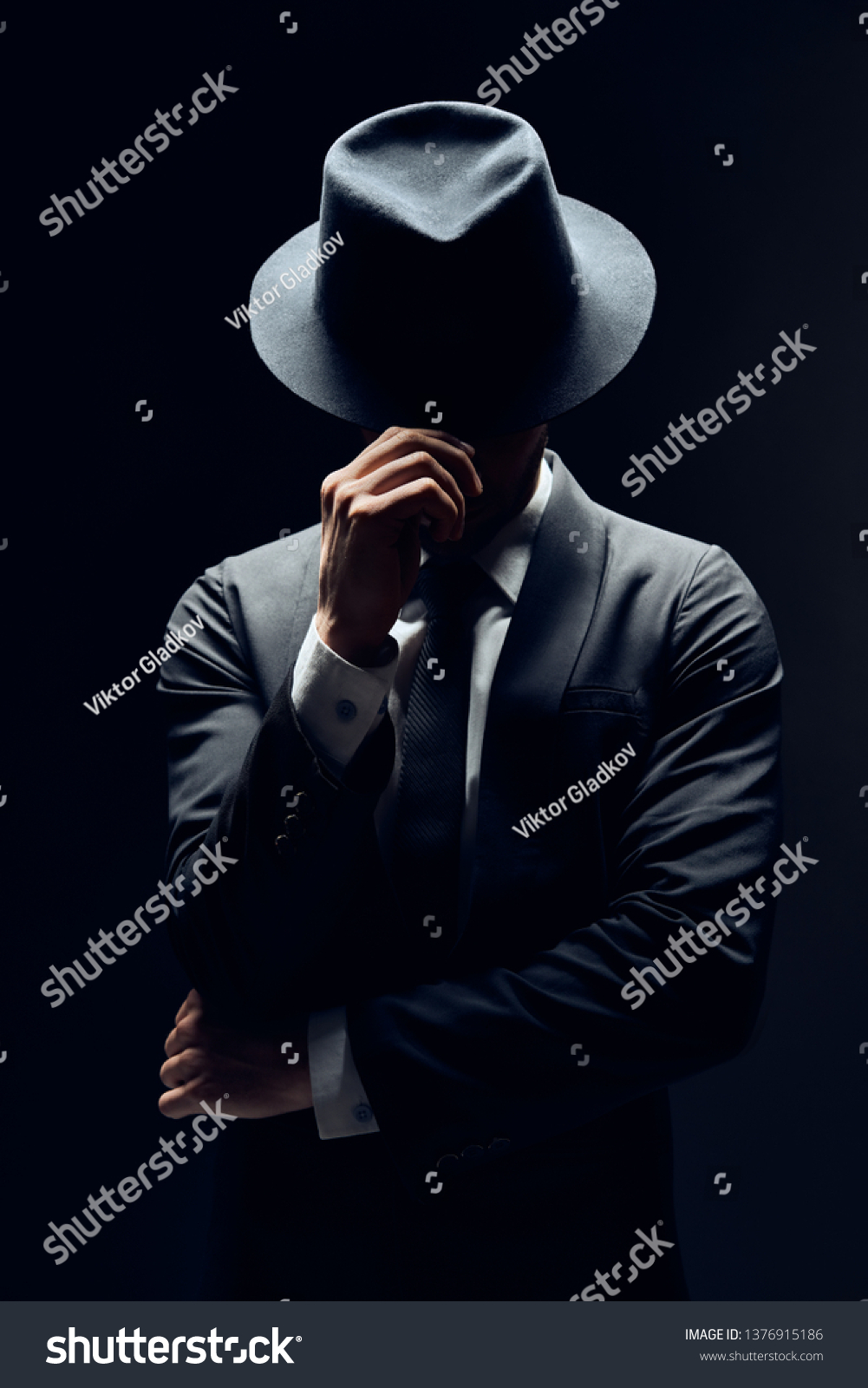 暗い背景にスーツを着た男性が帽子の後ろに顔を隠す 秘密の秘密のコンセプト の写真素材 今すぐ編集