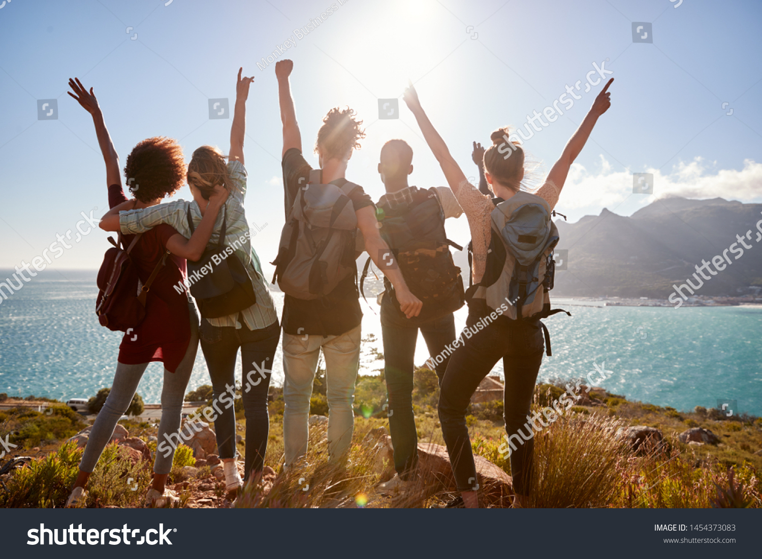 a group of young people are standing on top of a hill with their arms in the air .