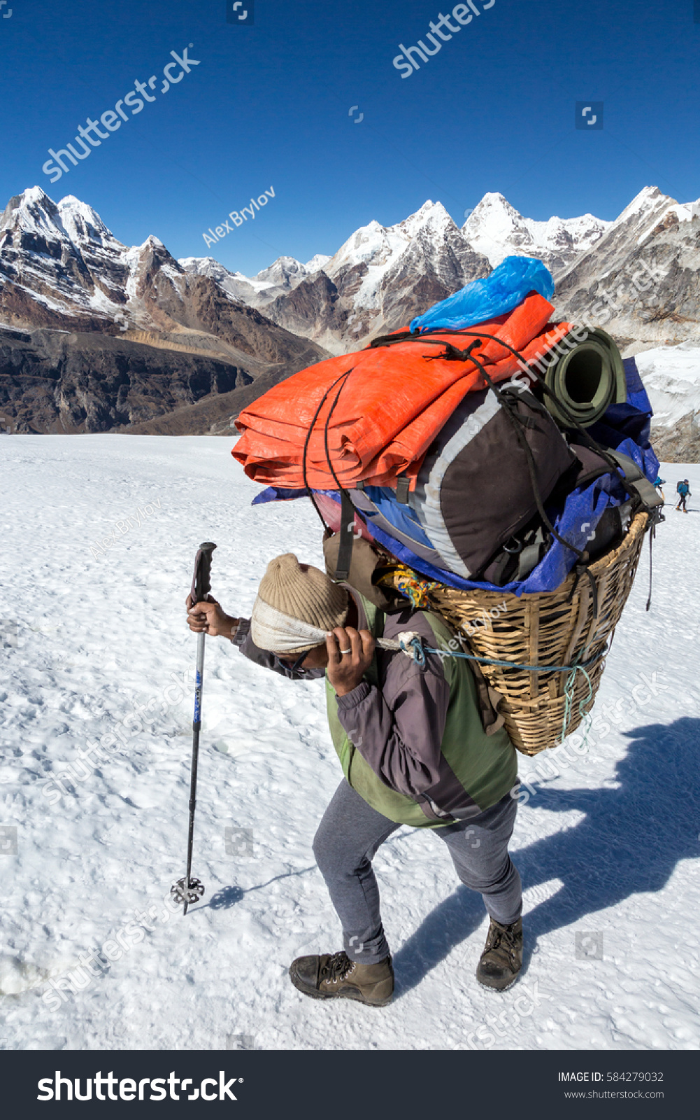 stock-photo-nepalese-sherpa-porter-walking-on-glacier-with-trekking-pole-carrying-basket-with-lots-of-mountain-584279032.jpg