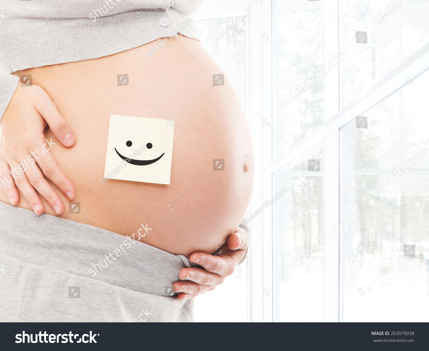 Pregnant Belly In Front Of A Window. Sticker With A Smiley On A Navel