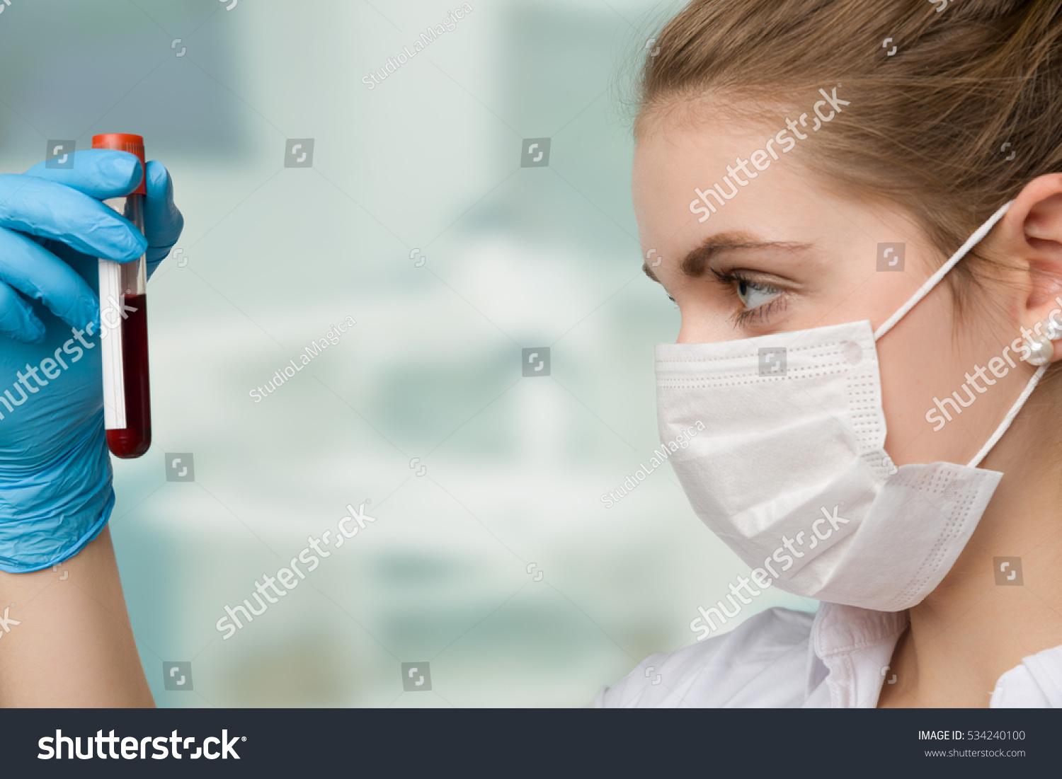 pretty nurse with face mask is holding a blood sample in a laboratory 