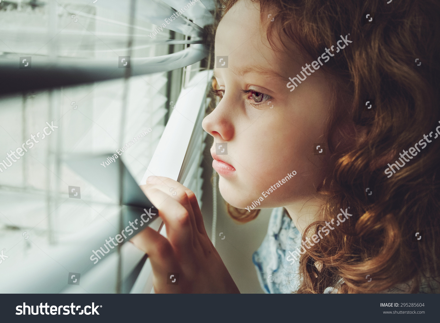 Sad Little Girl Looking Out The Window Through The Blinds. Background ...