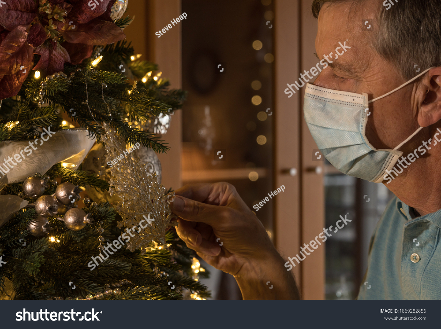 Senior lonely man with facemask looks at a lit christmas tree and recalls happier times before the pandemic
