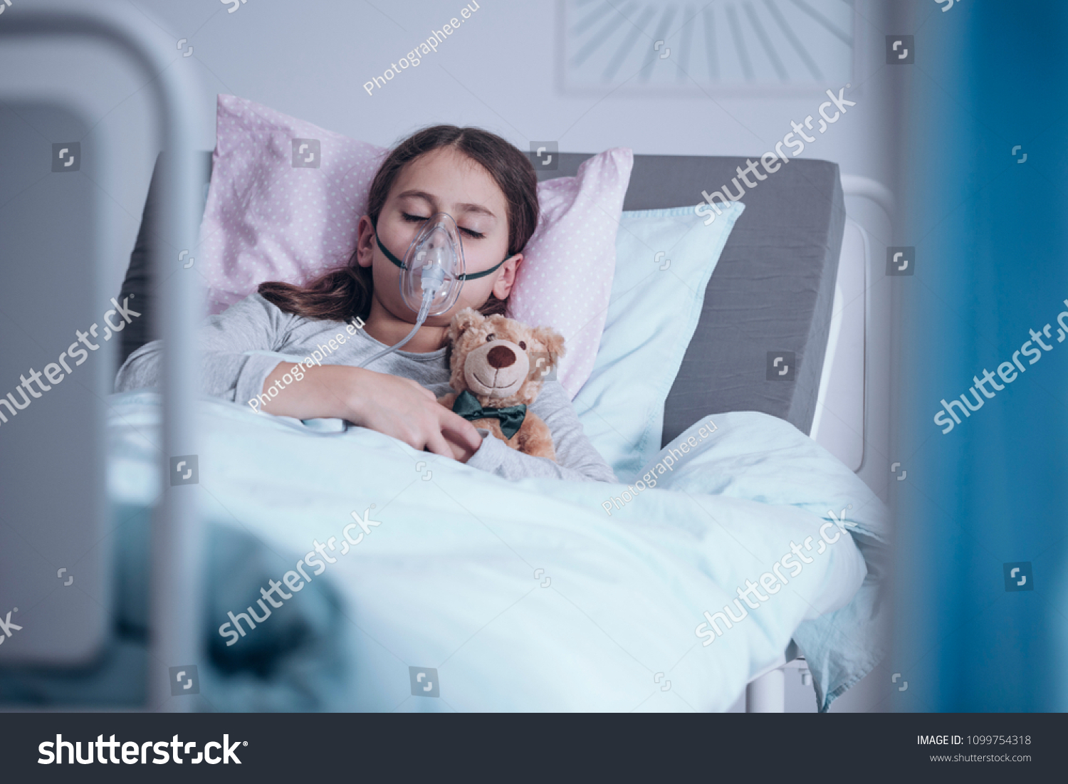 テディベアと一緒に病院のベッドで眠る酸素マスクを持つ病気の女の子 の写真素材 今すぐ編集