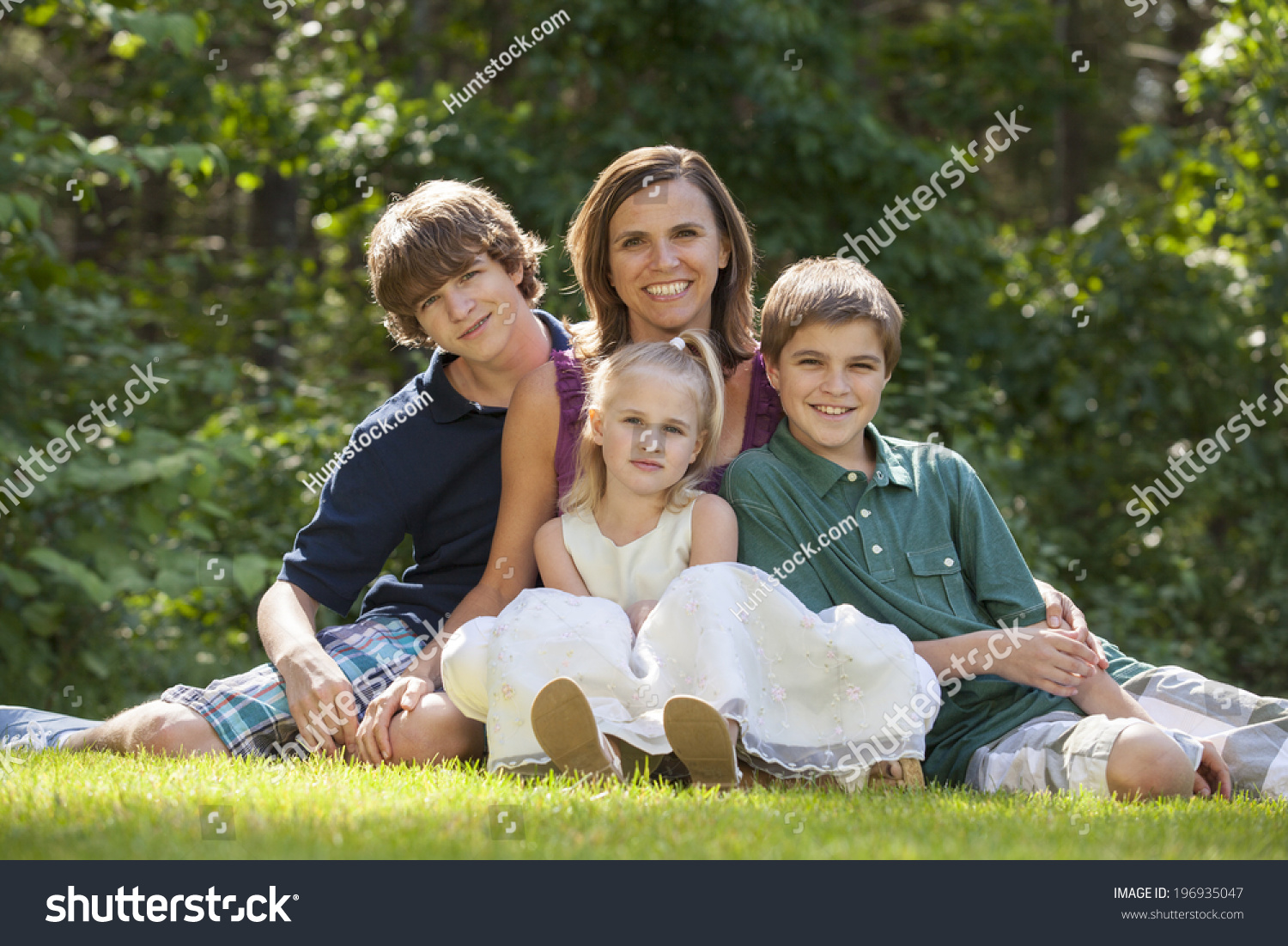 Single Parent Family With Three Children Sitting On Grass Lawn And ...