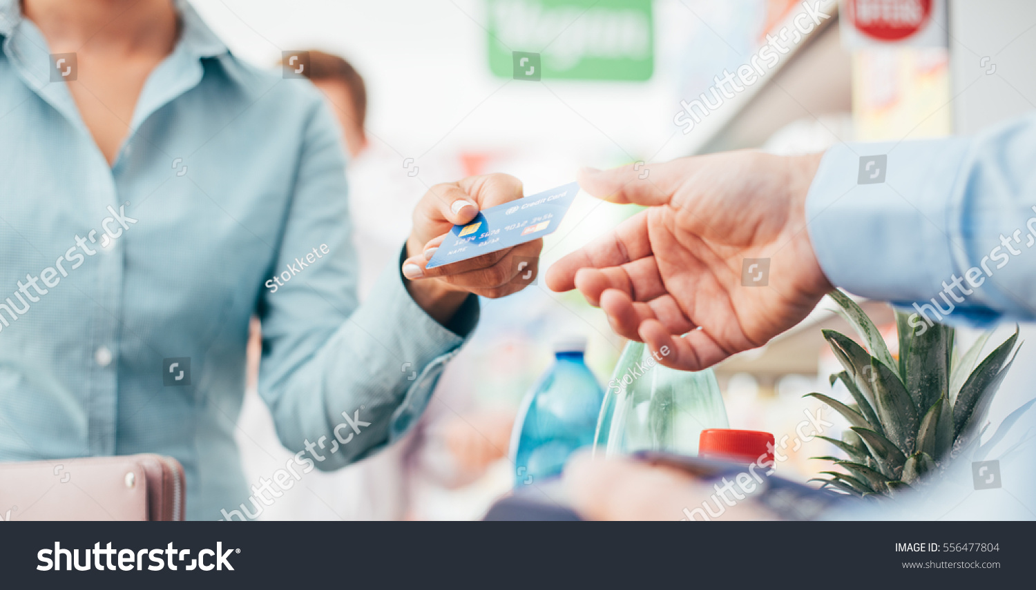 A woman is giving a credit card to a man in a supermarket.