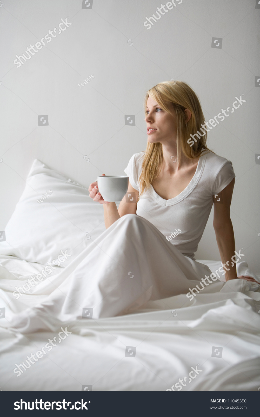 Woman Sitting Up In Bed With White Sheets And Holding A Cup Of Coffee ...