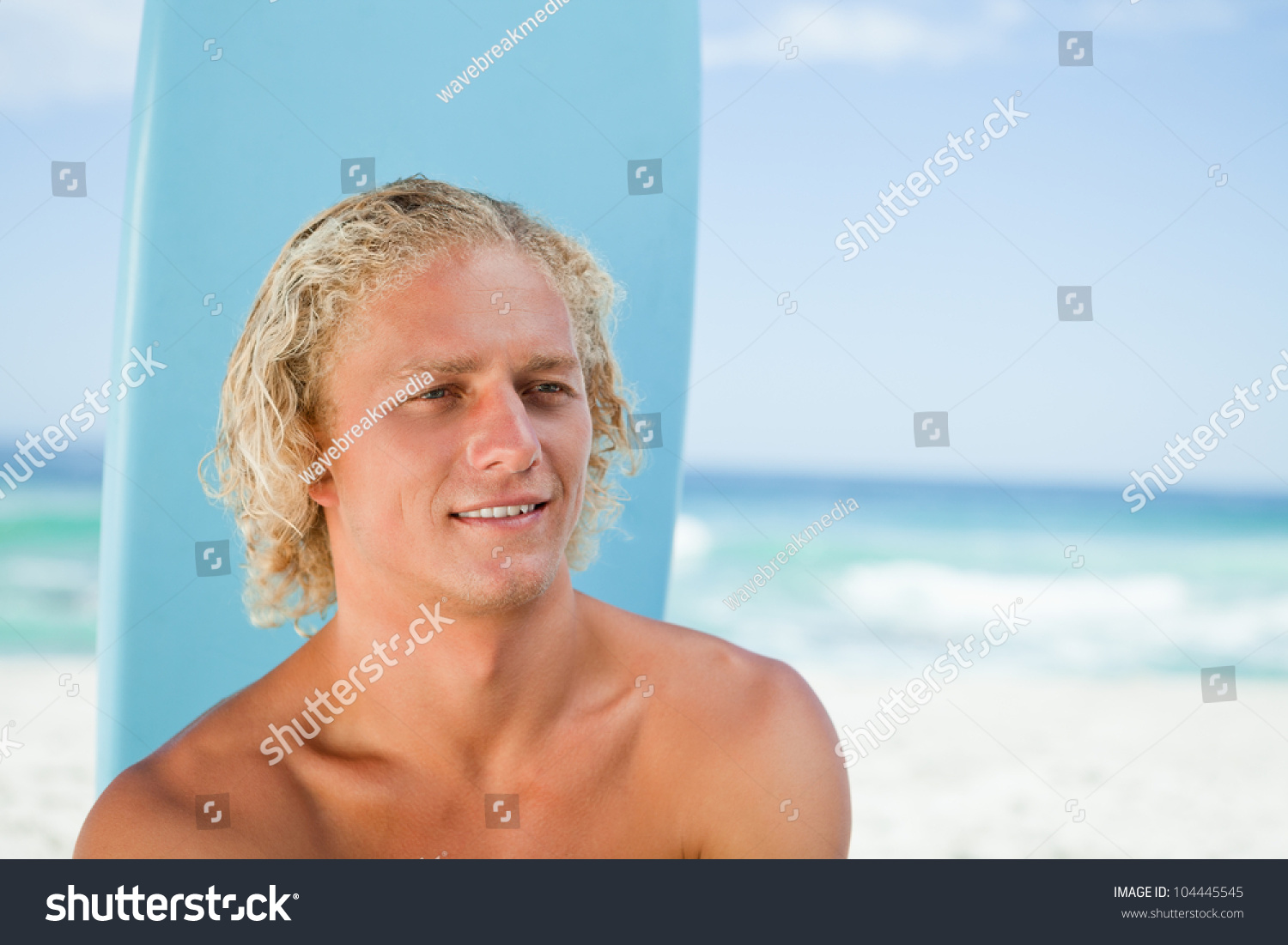 Young Blonde Man Sitting On The Beach With His Surfboard While Showing ...