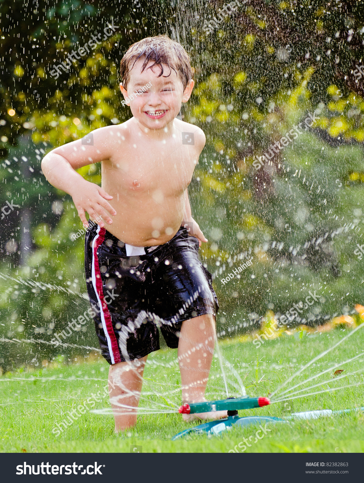 Young Boy Or Kid Cools Off By Playing In Water Sprinkler At Home In His ...