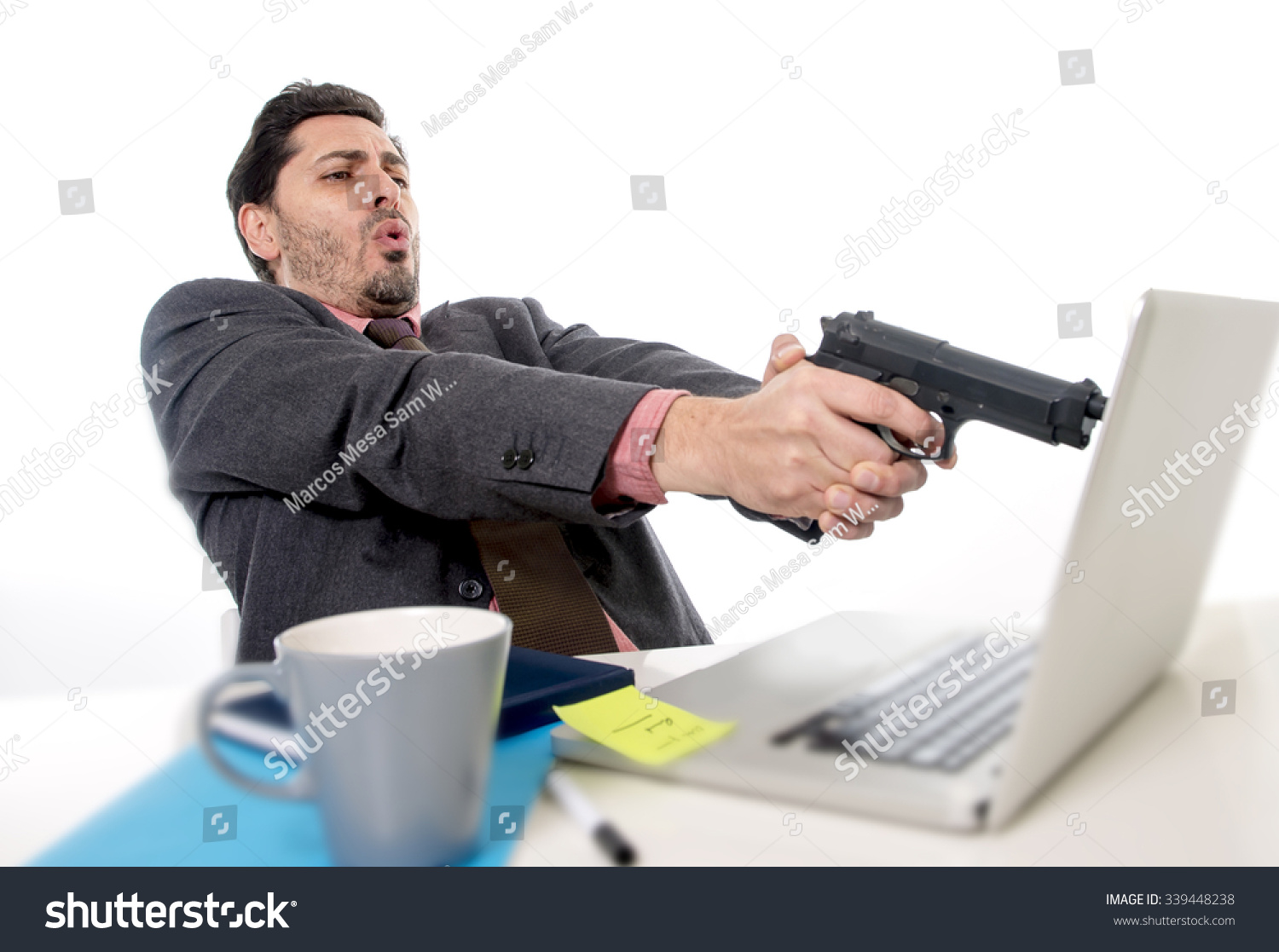 stock-photo-young-businessman-in-suit-and-tie-sitting-at-office-desk-working-on-computer-pointing-gun-to-339448238.jpg