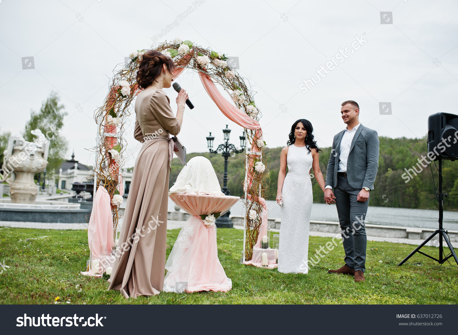 stock photo young fashionable lovely couple with speech master of wedding ceremony against decor arch on 637012726