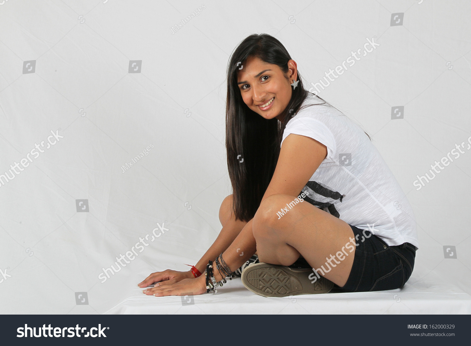 Young Indian Woman Sitting With Legs Crossed In Studio With White Background Young Indian Woman Sitting With Legs Crossed In Studio With White Background