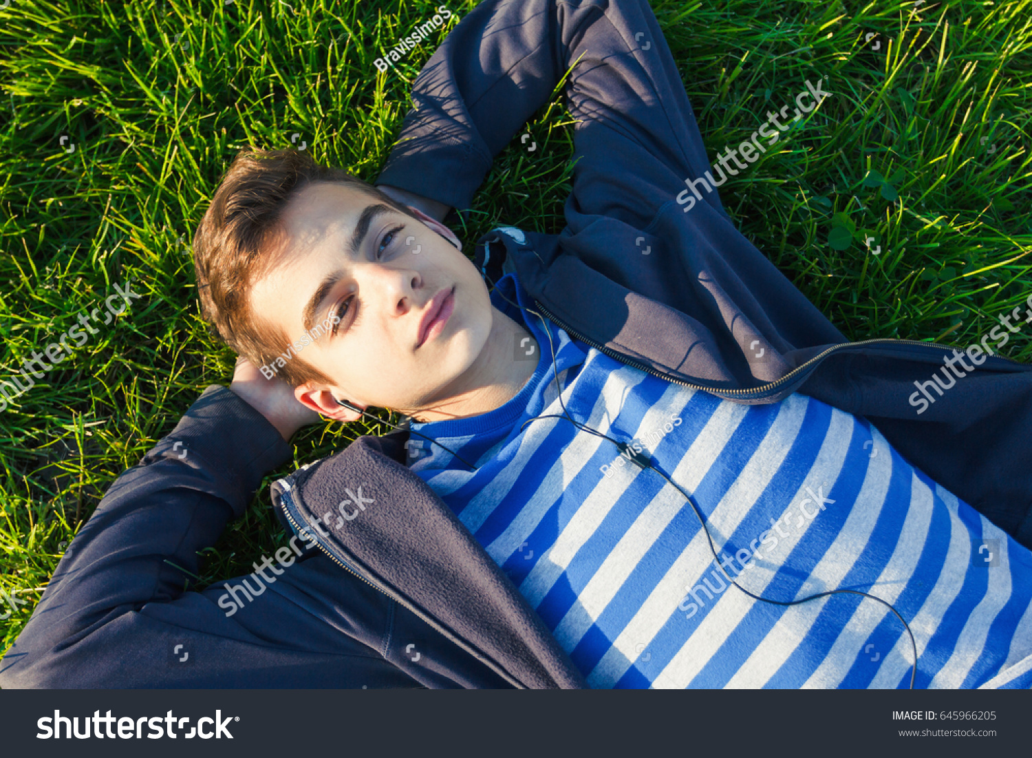 Young man listening music from smart phone on the grass in the park