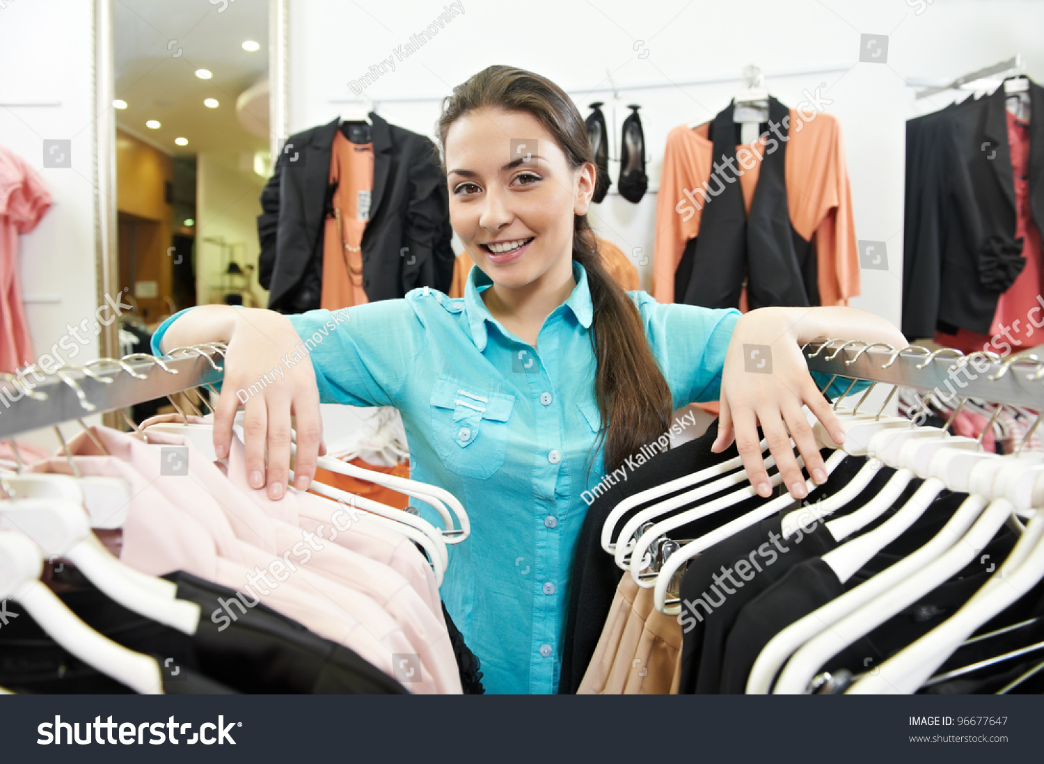 Young Smiling Woman Seller Assistant With Hands On Clothing Hangers At ...