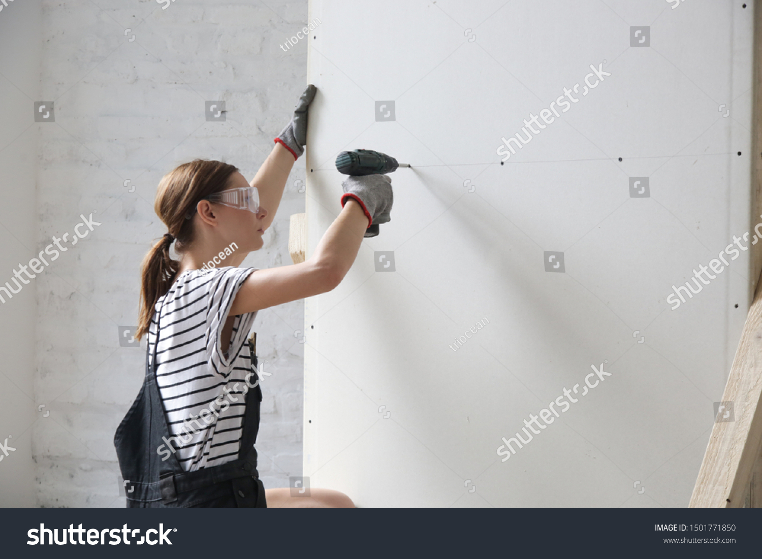 Young Woman Drilling Screws Into Plasterboard Stock Photo