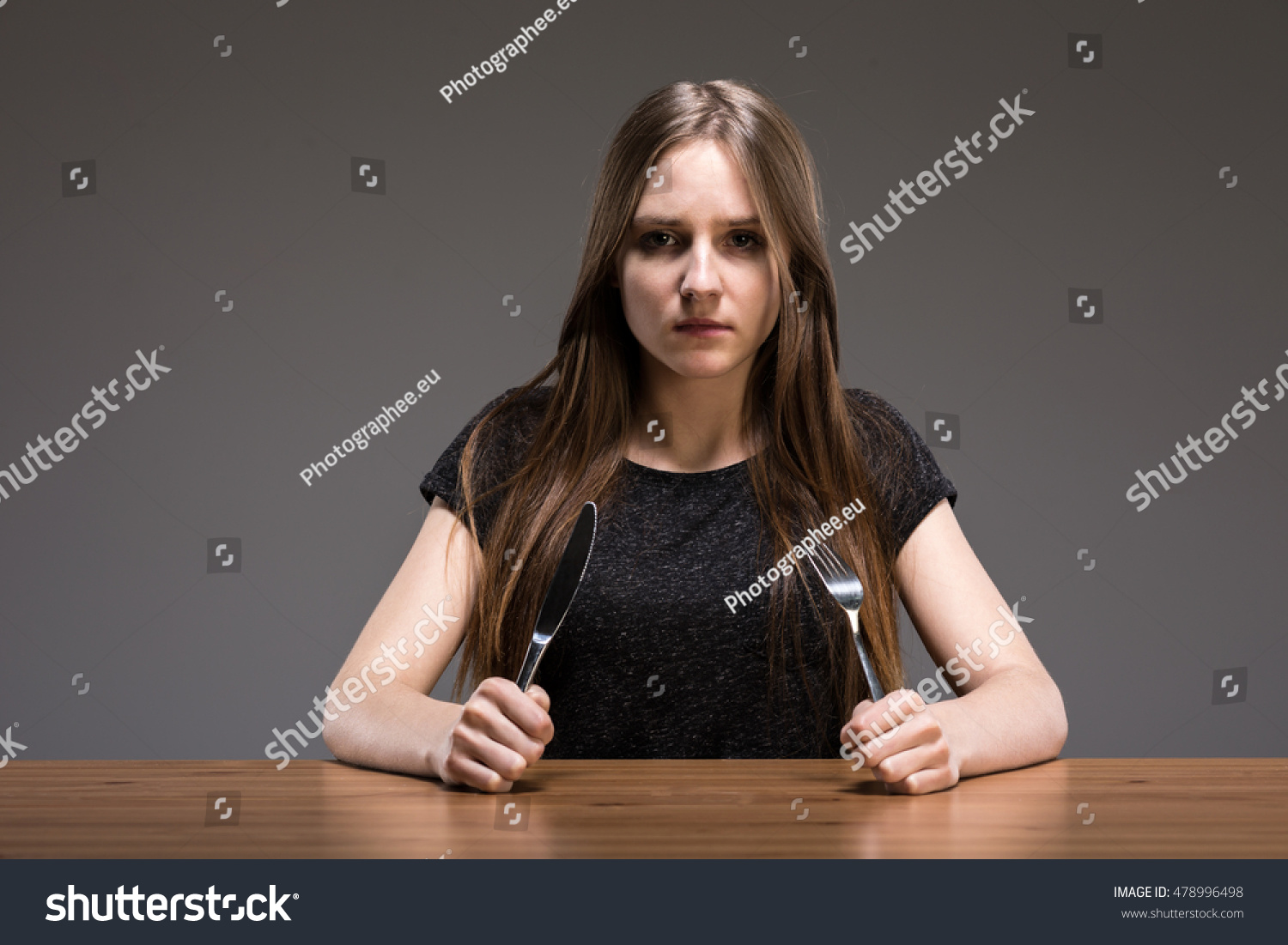 Young Woman Sitting At The Wooden Table With Cutlery In Her Hands Stock