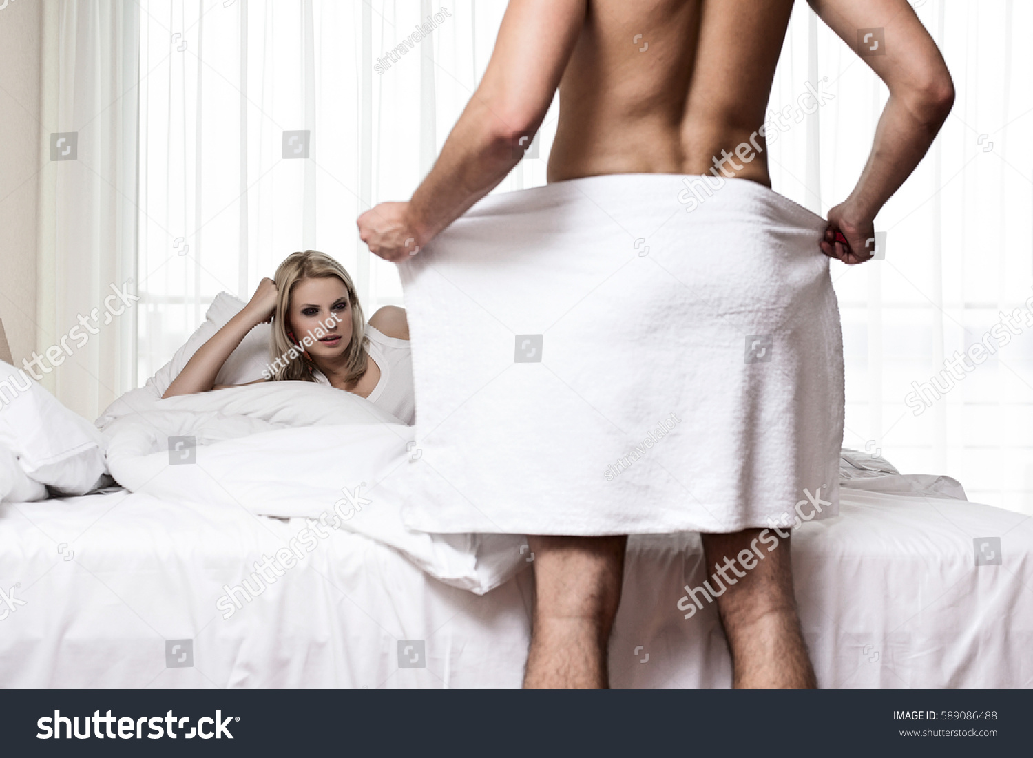 Young Woman Staring At Naked Man Holding Towel In Bedroom 
